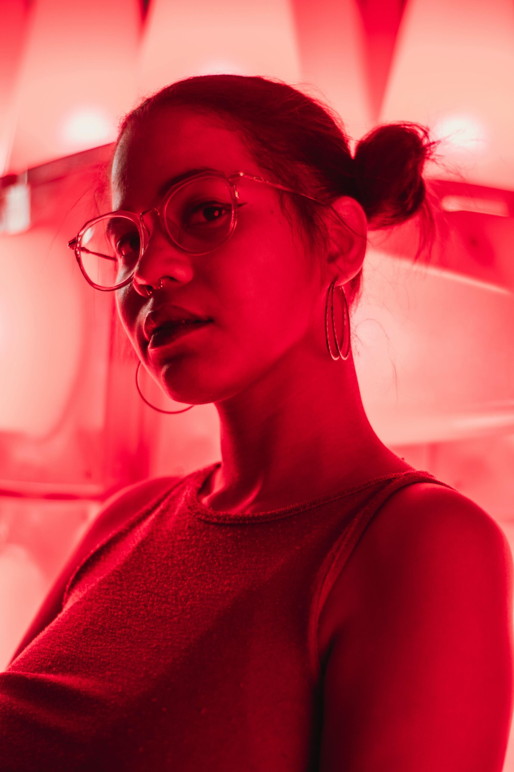 Portrait of a woman with glasses and earrings in dramatic red lighting.